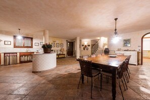 Een ruime keuken met een groot eiland, een eetgedeelte met een houten tafel en stoelen, en een trap naar een hoger gelegen verdieping.