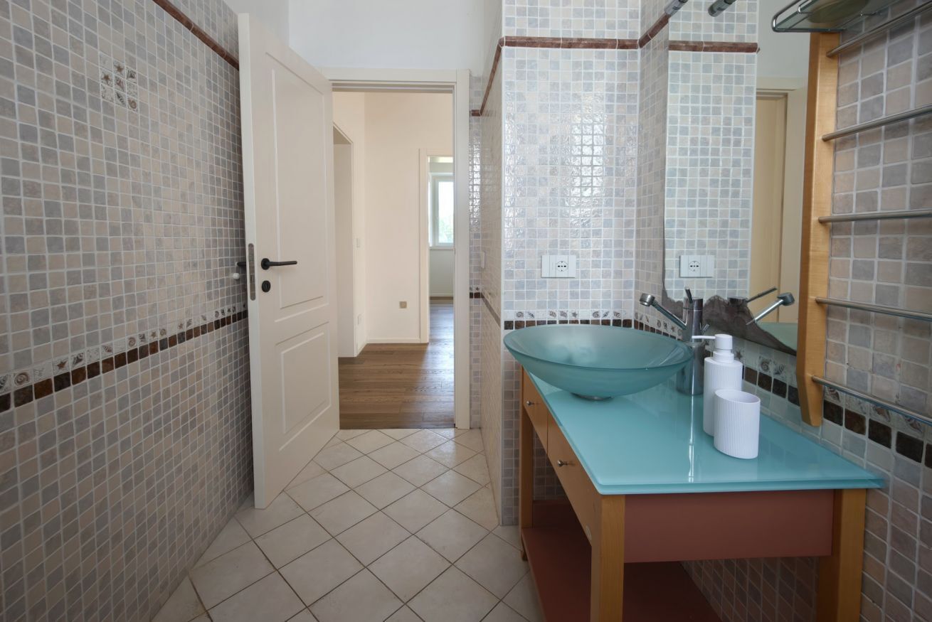A bathroom with a glass sink, tiled walls, and a wooden vanity.