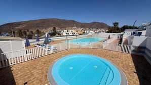 Un espace piscine sur le toit, comprenant deux piscines, des rampes blanches et une vue sur les bâtiments et les collines environnants.