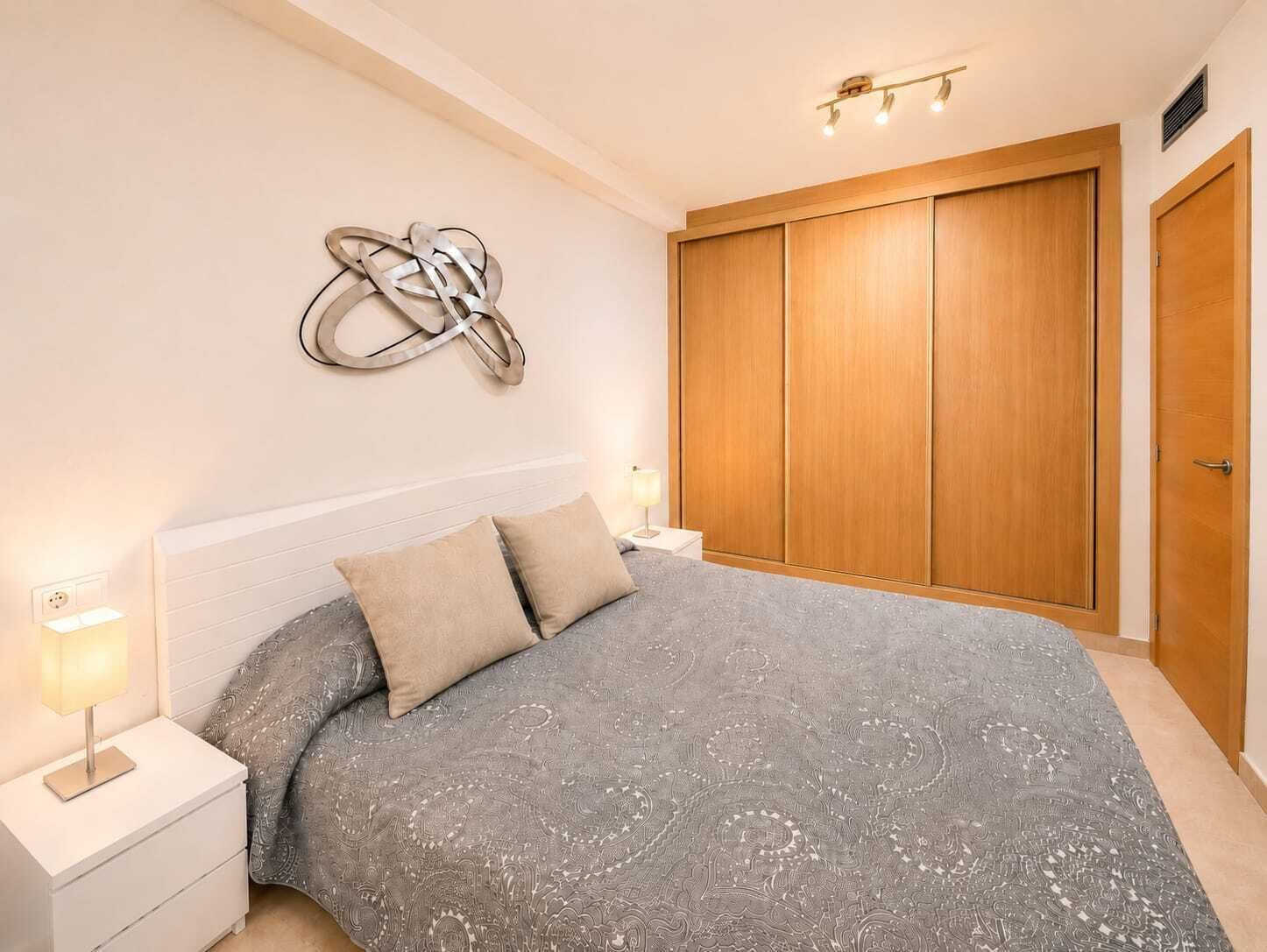 A bedroom with a bed, nightstands, a wall art piece, a wardrobe, and a door.