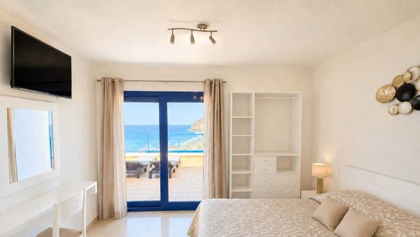 Une chambre avec un lit, une télévision, une armoire et une vue sur la plage.