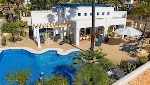 Eine moderne Villa mit Schwimmbad, Liegestühlen und einer  überdachten Sitzgruppe im Freien.