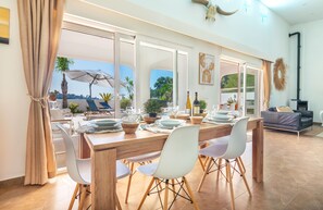 A dining area with a wooden table set for four, white chairs, and a view of the outdoors. - Exceptional Villa with Sea Views, Heated Pool, and Inspiring Design (La Sabatera)