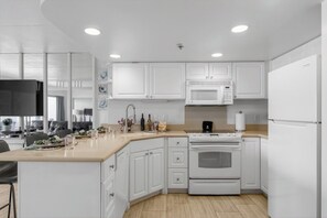 Eine moderne Küche mit weißen Schränken, einer Mikrowelle, einem Backofen und einer Kaffeemaschine.
