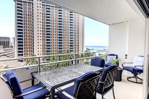 A balcony with a table and chairs, overlooking a high-rise building and a beach. - Ilikai Luxury Suites | 1-Bd Panoramic Ocean View w Free Parking & Car with 6 nights | ILK-732 by KBM (Honolulu)