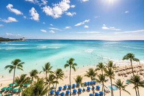 Ein Strand mit klarem türkisblauem Wasser, Palmen und Strandstühlen.