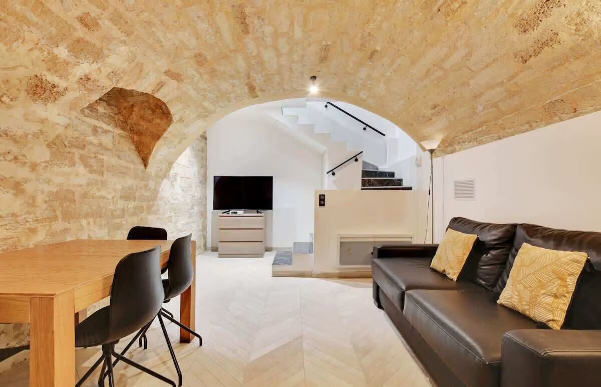 Un interior con comedor, sofá, televisor y escalera que sube a un nivel superior.