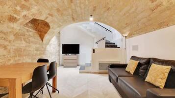 Un interior con comedor, sofá, televisor y escalera que sube a un nivel superior.