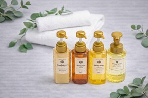 Four bottles of personal care products on a surface with a white towel and green leaves in the background. - Seven Residence Nipponbashi (Osakashi,chuoku,nipponbashi)