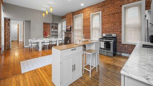 A modern kitchen with a brick wall, wooden flooring, and white cabinetry. - Walk to Allentown With Free Parking WFH Space (Buffalo)