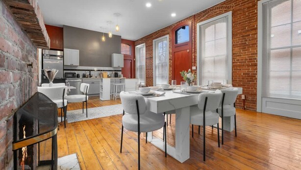 A modern kitchen with white cabinets, a dining area with a white table and chairs, and a brick wall. - Walk to Allentown With Free Parking WFH Space (Buffalo)