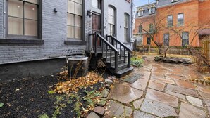 A building with a brick exterior, a stone pathway, and a small garden area with leaves. - Walk to Allentown With Free Parking WFH Space (Buffalo)