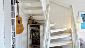 A staircase with white railings, a bookshelf with CDs and books, and a guitar leaning against it.