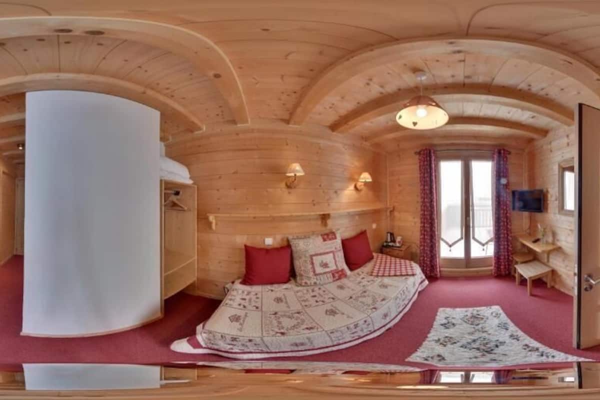 A wooden cabin interior with a bed, a large white cylindrical object, and a door leading to another room.