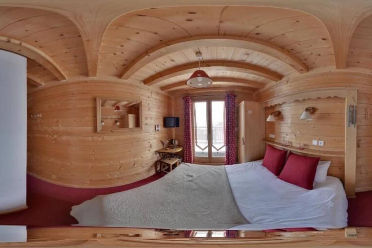 A wooden cabin room with a bed, a television, and a window with curtains.