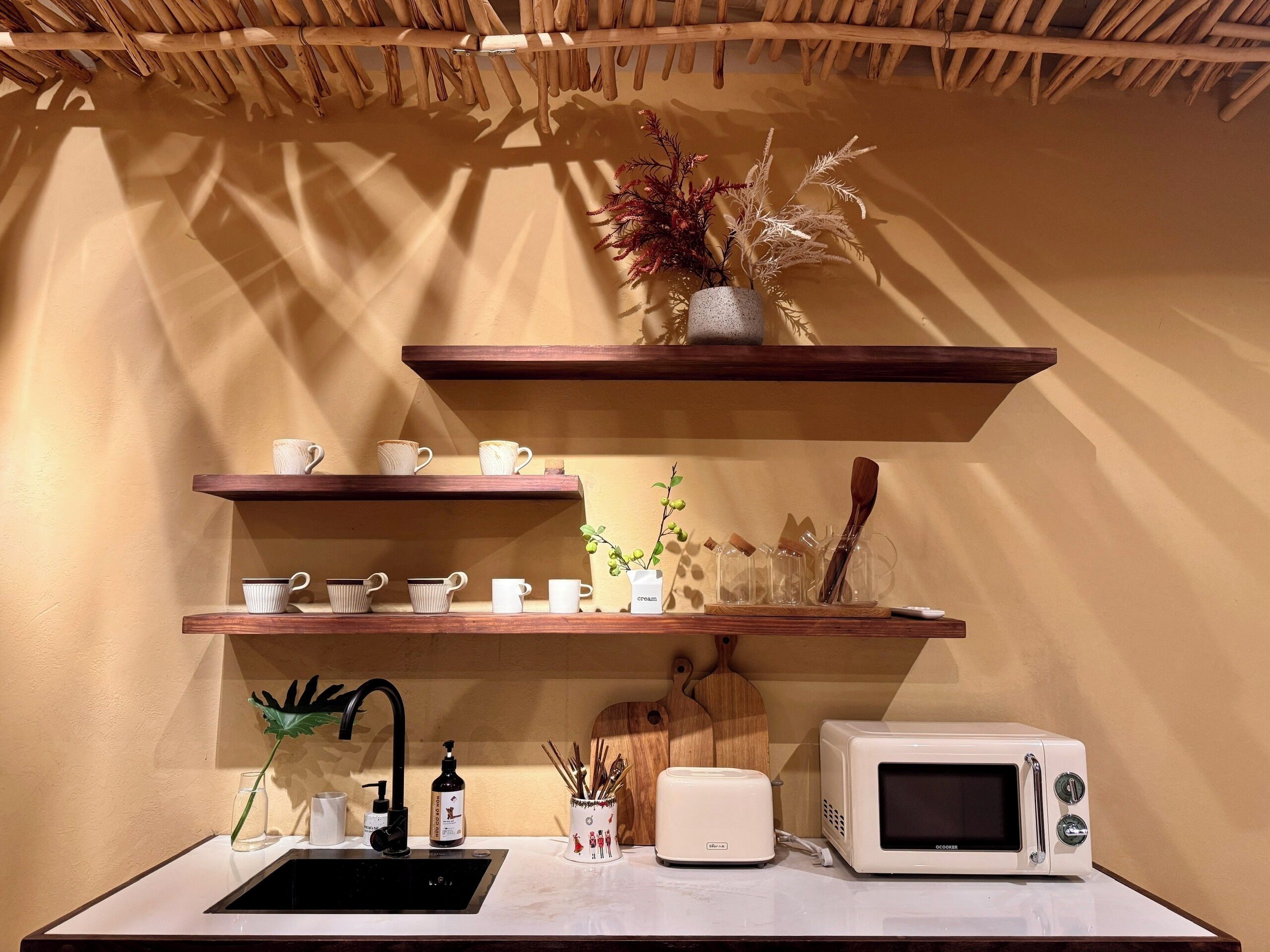 Una cocina con estantes de madera, microondas, tostadora, fregadero y una planta decorativa.