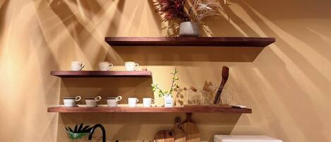 Una cocina con estantes de madera, microondas, tostadora, fregadero y una planta decorativa.