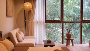 A room with a bed, a sofa, a hanging light fixture, a window with a view of trees, and a small table with a vase. - Hideout: Romantic Bathtub Escape at Old Quarter (Hà Nội)