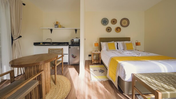 Ett kompakt hotellrum med en säng, ett sängbord, en lampa och ett litet pentry.