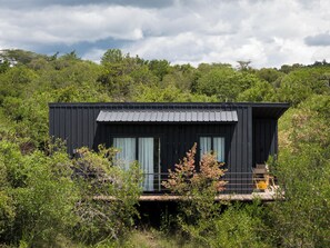 Una cabaña moderna negra con ventanas amplias, rodeada de abundante follaje y árboles.