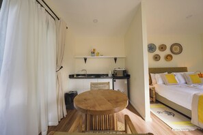Una habitación compacta con una cama, un pequeño espacio kitchenette, una mesa de comedor y una silla.
