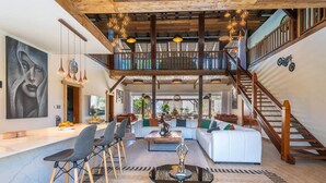 Un espacio habitable amplio con techo alto, vigas de madera, una escalera y un comedor con sillas y mesa.