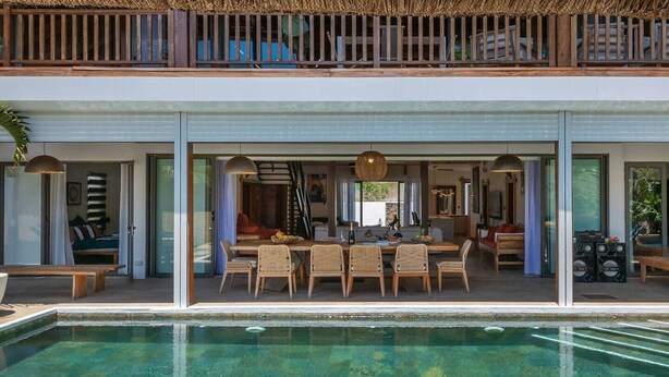 Una casa moderna con piscina, comedor y un balcón con techo de paja.