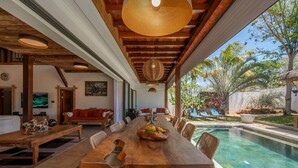 Un comedor amplio con una larga mesa de madera, sillas de mimbre y vistas a una piscina.
