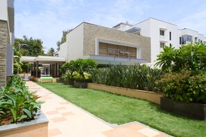 A modern building with a flat roof, a covered entrance, and a well-maintained garden with a paved walkway. - Luxe 2BHK Private Garden Flat by ORR Tech Parks (Bengaluru)