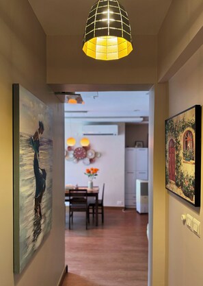 A hallway with a dining area, a kitchen, and artwork on the walls. - Luxe 2BHK Private Garden Flat by ORR Tech Parks (Bengaluru)