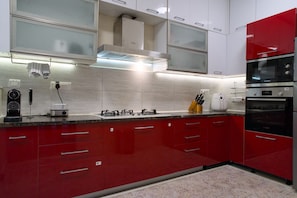 A modern kitchen with red cabinets, stainless steel appliances, and a built-in oven. - Luxe 2BHK Private Garden Flat by ORR Tech Parks (Bengaluru)