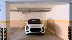 Valkoinen auto oli pysäköitynä pysäköintihalliin, jonka seinät oli koristeltu mustilla ja keltaisilla raidoilla ja jonka lattia oli betonia.