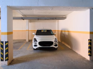 A white car parked in a parking garage with yellow and black striped walls and a concrete floor. - Luxe 2BHK Private Garden Flat by ORR Tech Parks (Bengaluru)