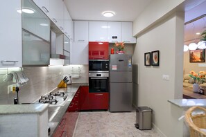 A modern kitchen with white cabinets, a red appliance, stainless steel appliances, and a trash bin. - Luxe 2BHK Private Garden Flat by ORR Tech Parks (Bengaluru)