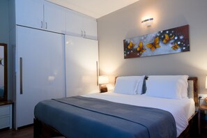 A hotel room with a bed, a nightstand, a lamp, a wardrobe, and a painting on the wall. - Luxe 2BHK Private Garden Flat by ORR Tech Parks (Bengaluru)