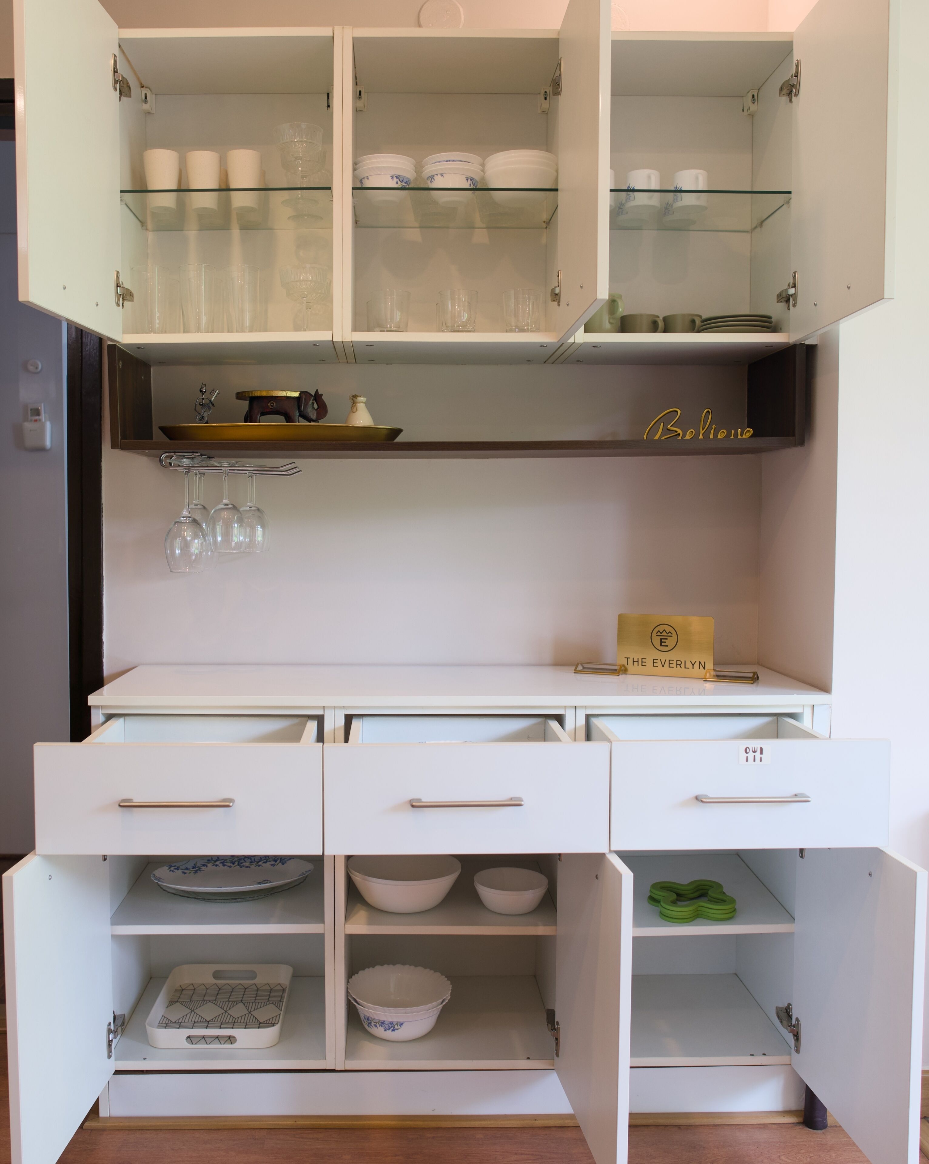 A kitchen with open cabinets displaying dishes, glasses, and a coffee machine.