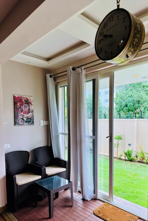 Quarto com porta de correr de vidro, móveis de vime, relógio de parede e quadro emoldurado.
