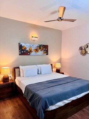 Quarto de hotel com cama, luminárias de cabeceira, ventoinha no teto, luz acoplada à parede e pintura de borboleta.