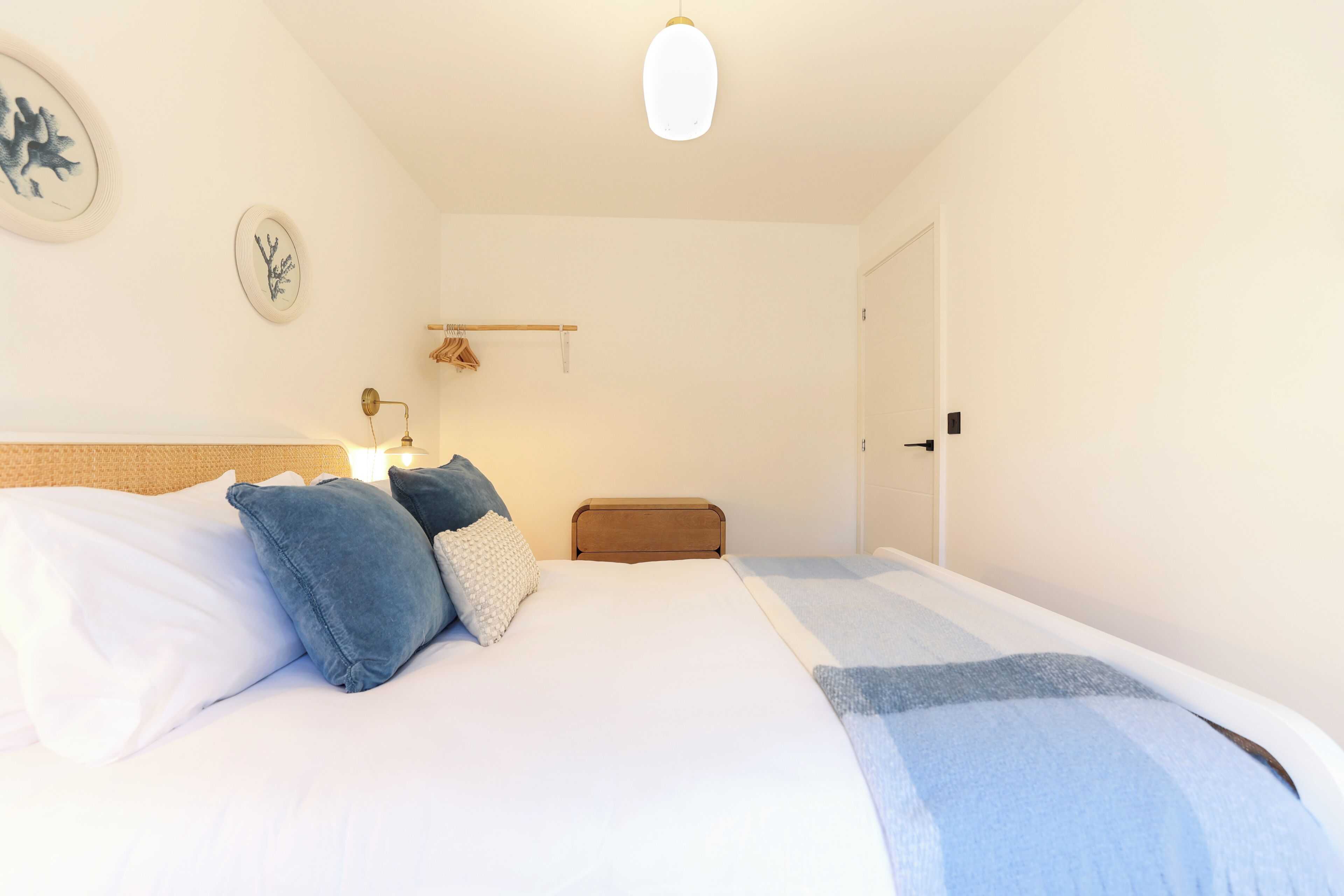 A bedroom with a bed, pillows, a bedside table, a lamp, a wall clock, and a door.