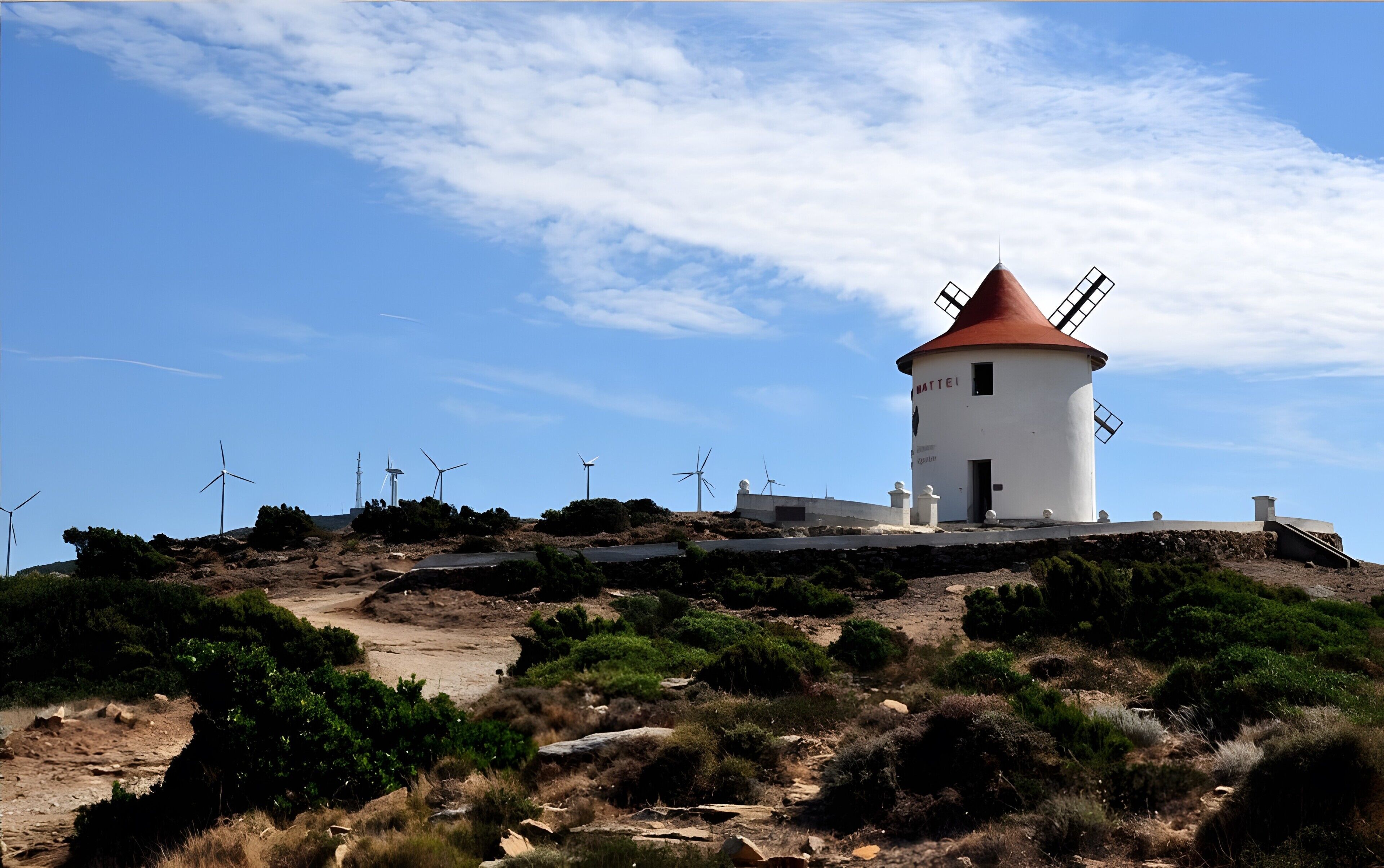 Un faro con techo rojo y aerogeneradores al fondo.