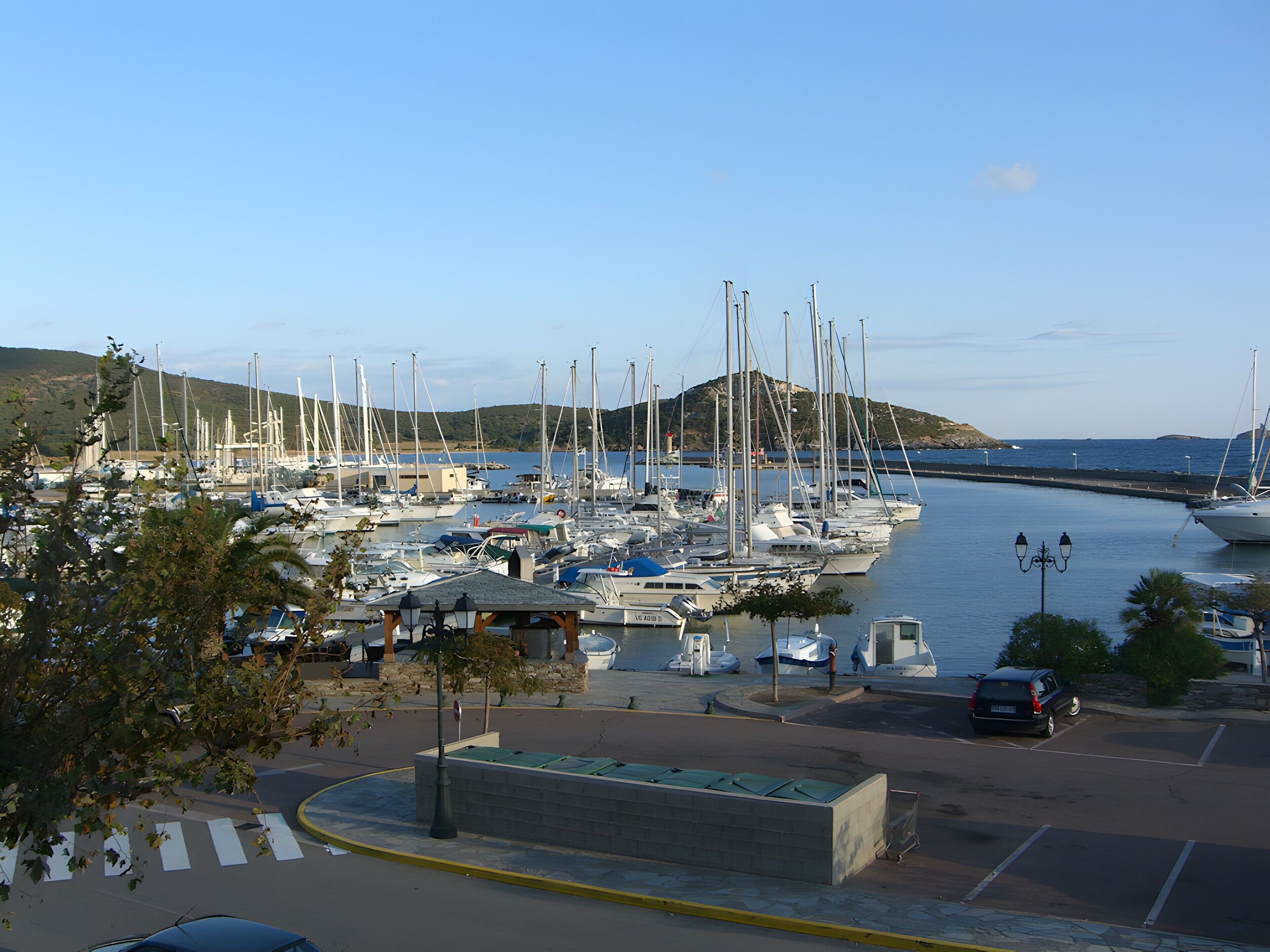 Un puerto deportivo con barcos amarrados, una zona de estacionamiento y vista al agua.