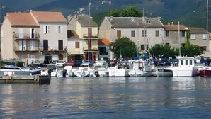 A marina with boats docked, buildings with balconies, and wind turbines in the background.