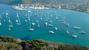 A marina with numerous sailboats docked, surrounded by hills and a small town in the background.