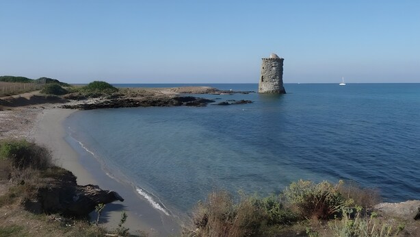 A coastal landscape with a stone tower, sandy beach, and calm sea.