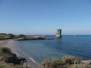 Eine Küstenlandschaft mit einem Stein Turm, Sandstrand und ruhiger See.