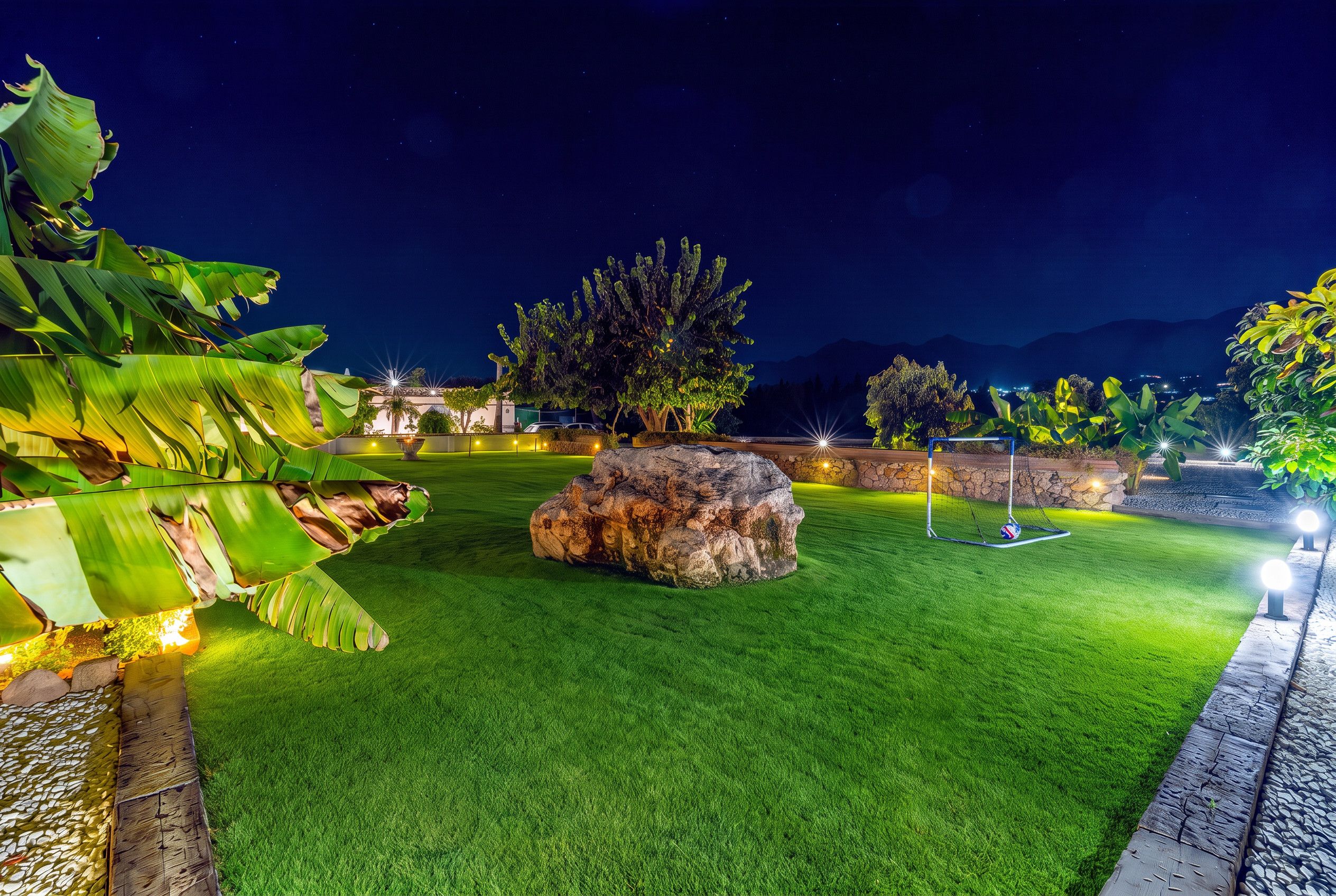 A well-maintained lawn with a rock centerpiece, a soccer goal, and a small pond with a waterfall.