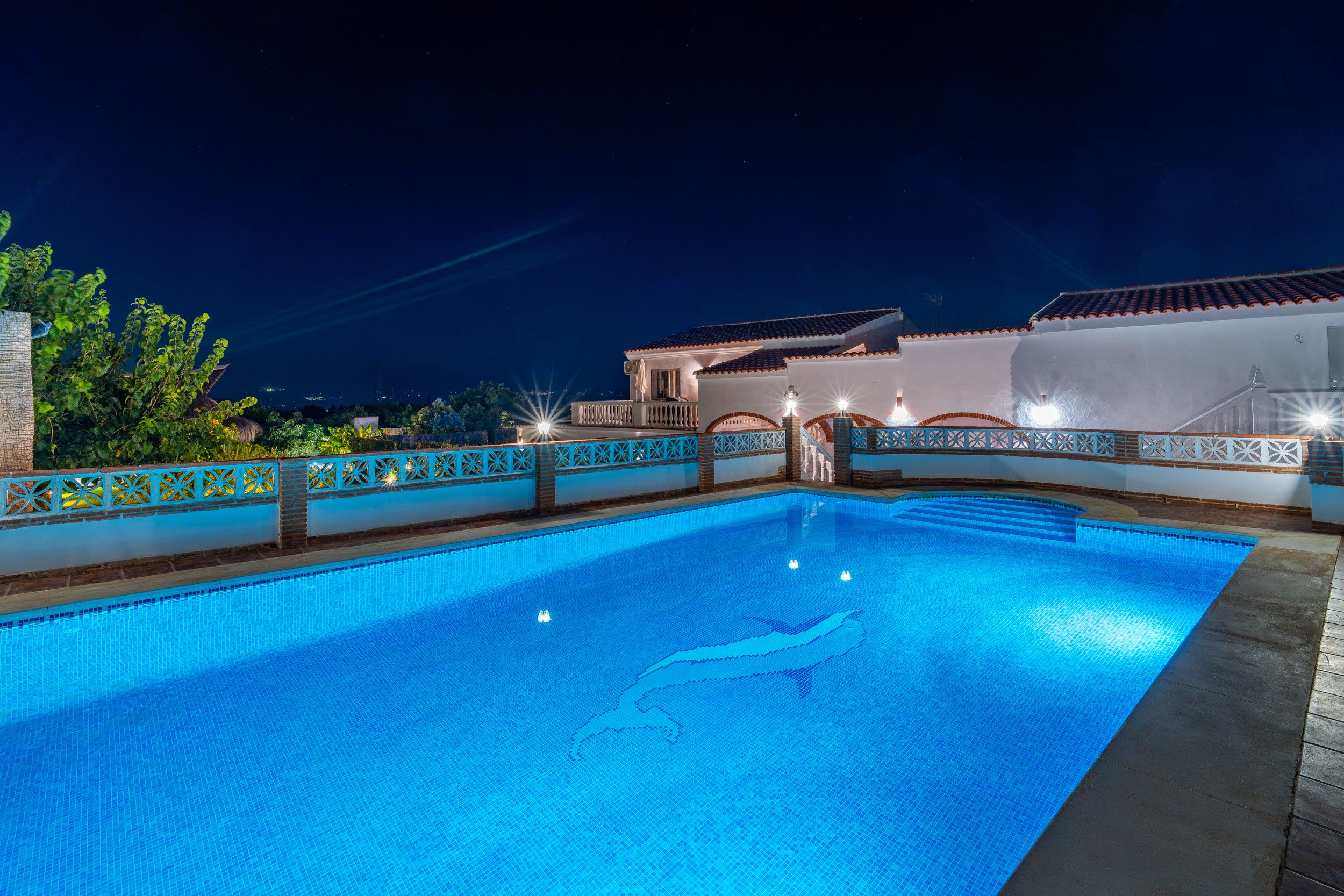 A swimming pool with a clear water surface, surrounded by a decorative fence with geometric patterns.