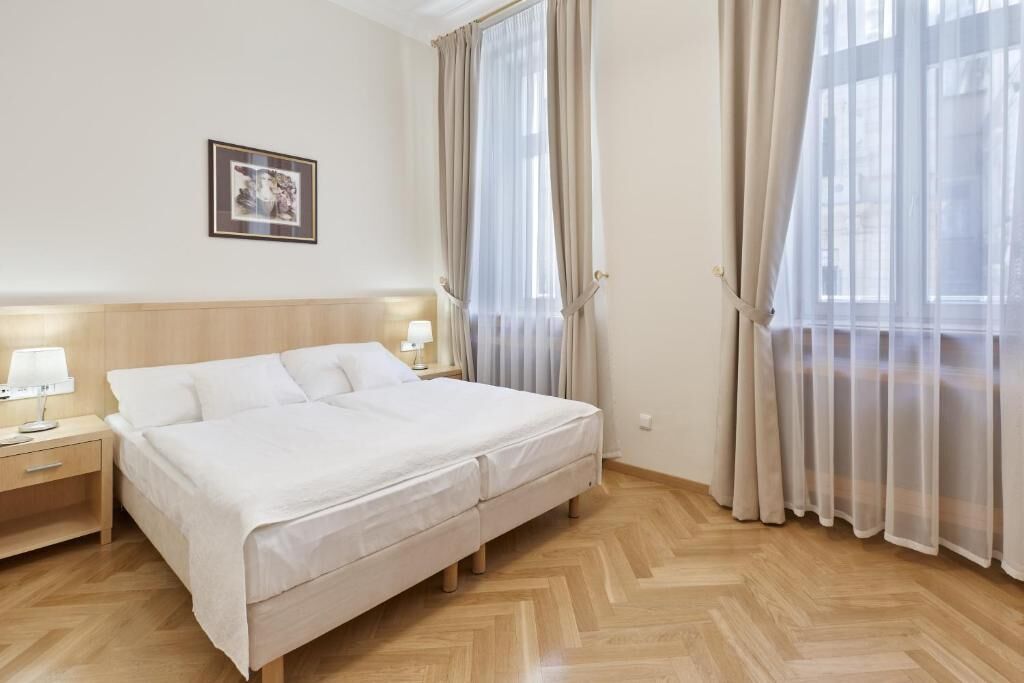 A hotel room with a bed, nightstands, a framed picture, and sheer curtains.