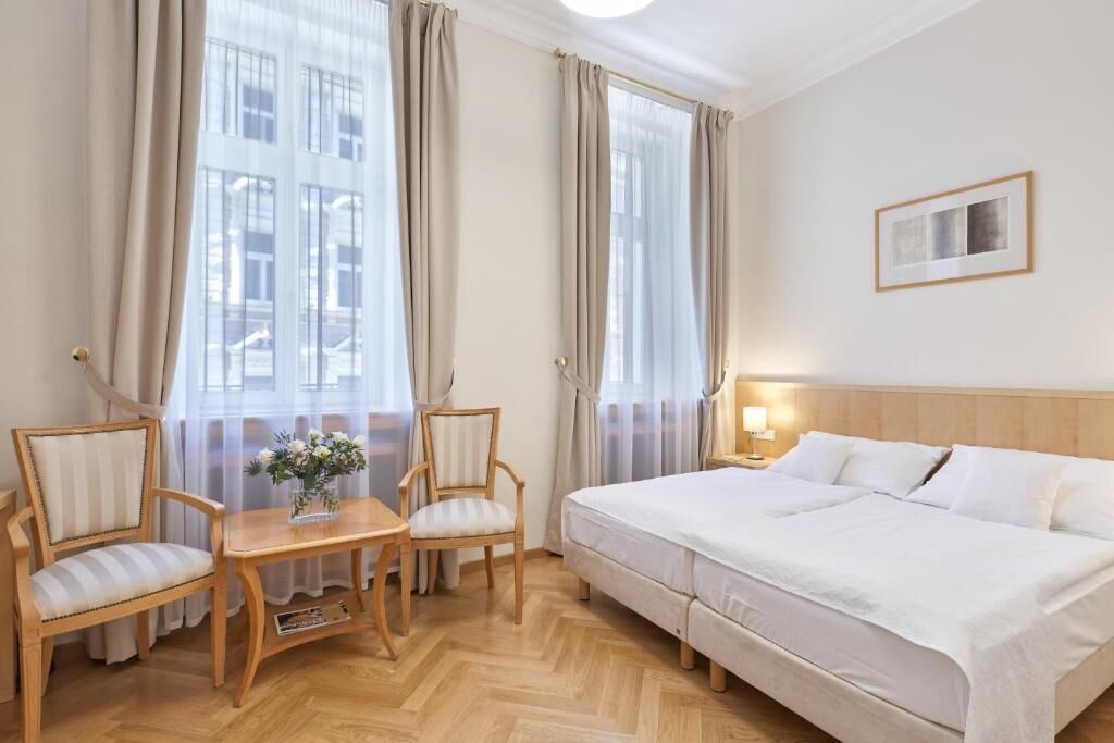A hotel room with a bed, two chairs, a small table, and a nightstand with a lamp.
