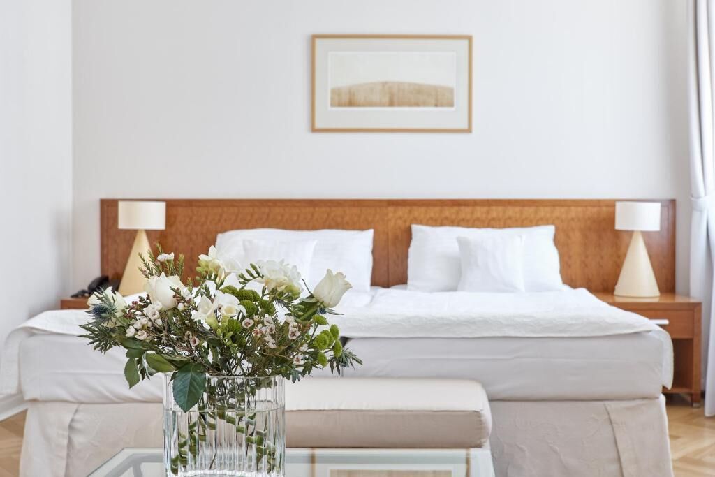 A hotel room with a bed, bedside tables, a vase with flowers, and a framed picture on the wall.